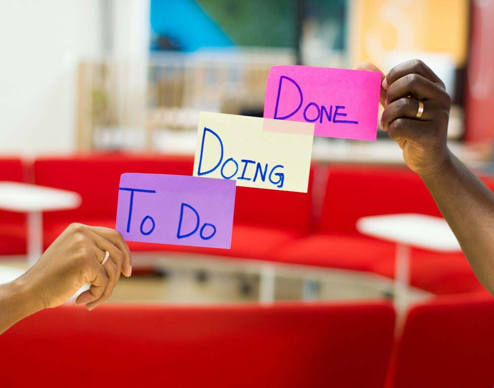 Hands holding To Do, Doing and Done sticky notes for a kanban workflow