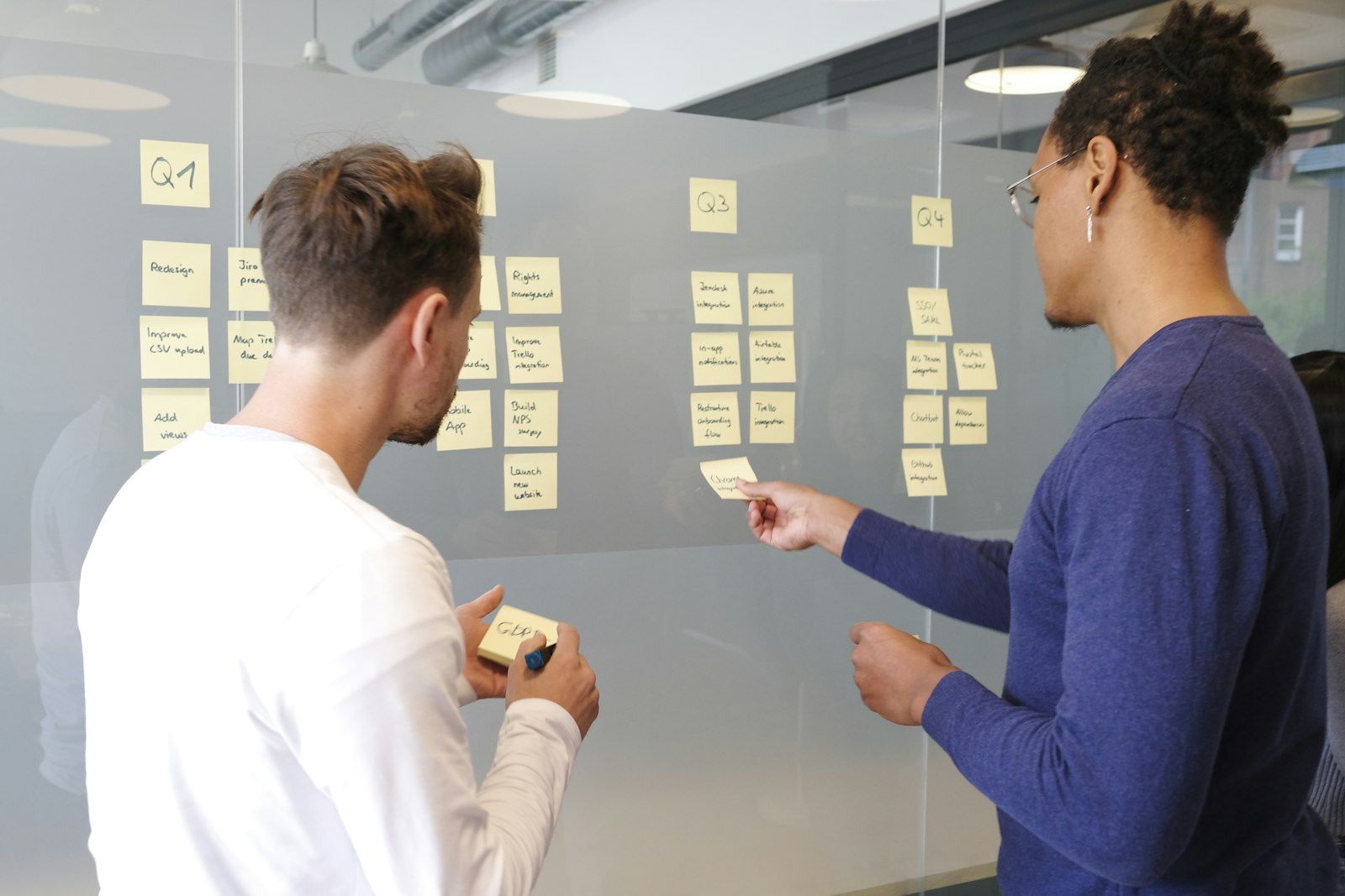 Two colleagues mapping a project plan with yellow sticky notes on a glass wall
