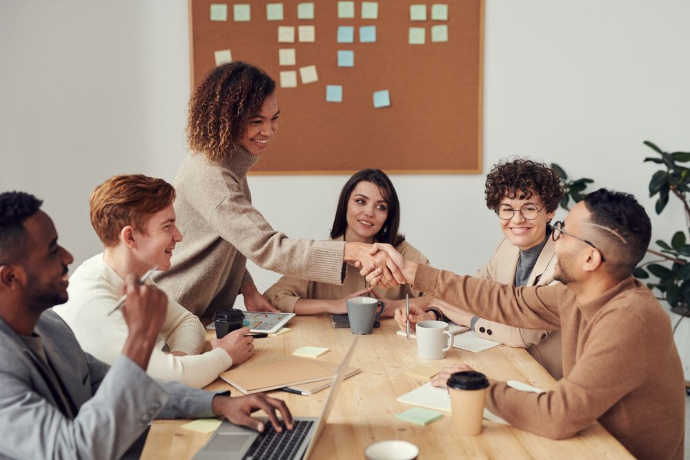 Team members shaking hands across a meeting table with laptops and notes