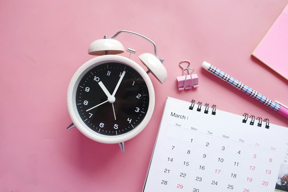 Alarm clock beside a monthly calendar and pen for time management